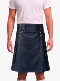 A person wearing a black faux-leather kilt with silver-tone metal hardware, including D-ring details and side pockets, paired with a light pink t-shirt against a plain white background.