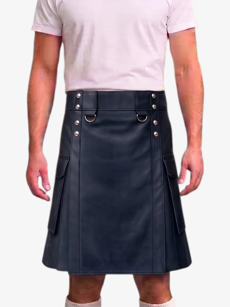 A person wearing a black faux-leather kilt with silver-tone metal hardware, including D-ring details and side pockets, paired with a light pink t-shirt against a plain white background.