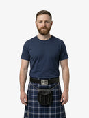Man wearing a navy blue t-shirt and plaid kilt on a white background