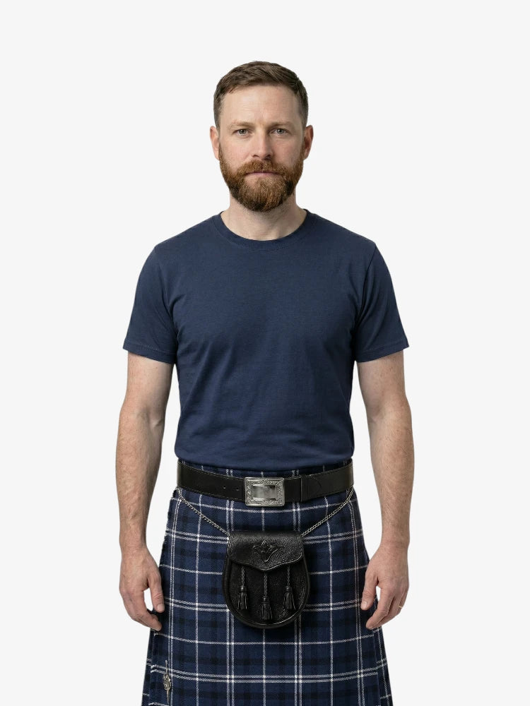 Man wearing a navy blue t-shirt and plaid kilt on a white background