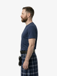 Man wearing a navy t-shirt and plaid kilt on a white background