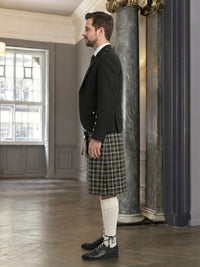 Man wearing a black jacket, plaid kilt, and white knee-high socks in an elegant room.