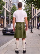 A man viewed from behind wearing an olive green leather kilt with lace-up back detailing, a white t-shirt, white knee-high socks, and black shoes, standing on a city sidewalk.