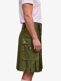 An olive green faux-leather kilt with pleated detailing, flap pockets, and brass snap buttons, shown on a model wearing a white t-shirt against a light gray background.