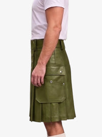 A side view of a person wearing an olive green faux-leather kilt with silver snap button details and pleated folds, paired with a white t-shirt against a light gray background.