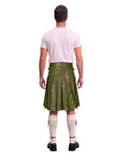 A man shown from the back wearing an olive green leather kilt, a light pink t-shirt, cream knee-high socks, and black shoes, against a solid white background.