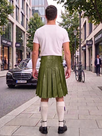 A man standing on a city sidewalk, viewed from behind, wearing an olive green leather pleated kilt, a white t-shirt, white knee-high socks, and black shoes. Buildings, trees, a black Mercedes, and a bicycle are visible in the background.