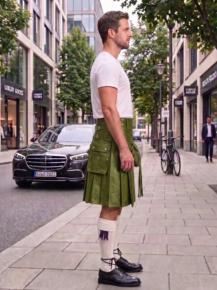 A man standing on a city sidewalk wearing a green leather kilt, white t-shirt, white socks, and black leather shoes, with a street scene in the background.