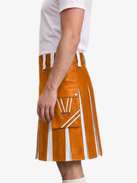 A side view of a model wearing a mustard orange faux-leather kilt with white contrast stitching, pleats, and a front utility pocket, paired with a white t-shirt.