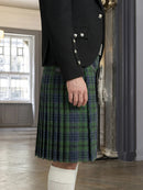Person wearing a black jacket with silver buttons and a green plaid kilt indoors.