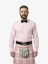 Man wearing a pink dress shirt, bow tie, and pink plaid kilt on a white background