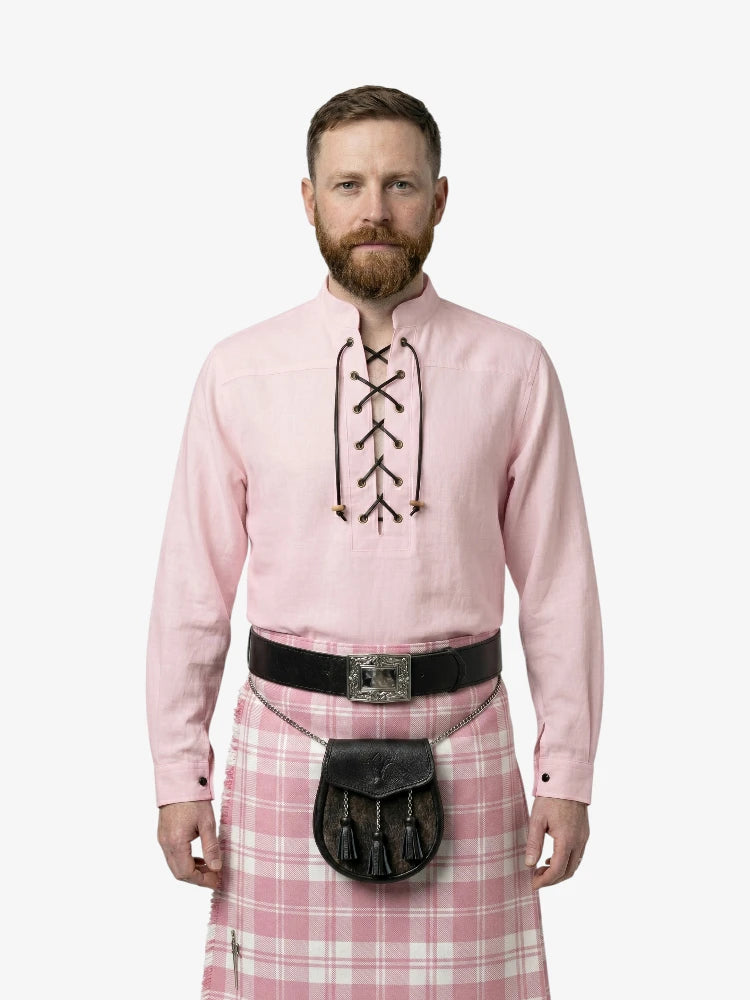 Man wearing a pink shirt with lace-up front and a pink plaid kilt on a white background