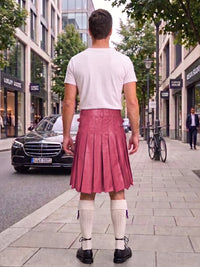 A man viewed from behind wearing a white t-shirt and a pink pleated faux-leather kilt, standing on a city sidewalk next to a street with a Mercedes-Benz car and trees.