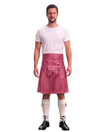 A man modeling a pink faux-leather kilt with a front pouch pocket, paired with a white t-shirt, cream knee-high socks, and black lace-up shoes, against a plain white background.