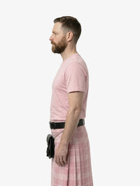 Man wearing a pink t-shirt and plaid kilt standing against a white background