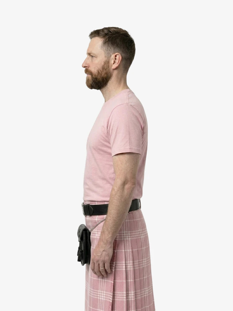 Man wearing a pink t-shirt and plaid kilt standing against a white background