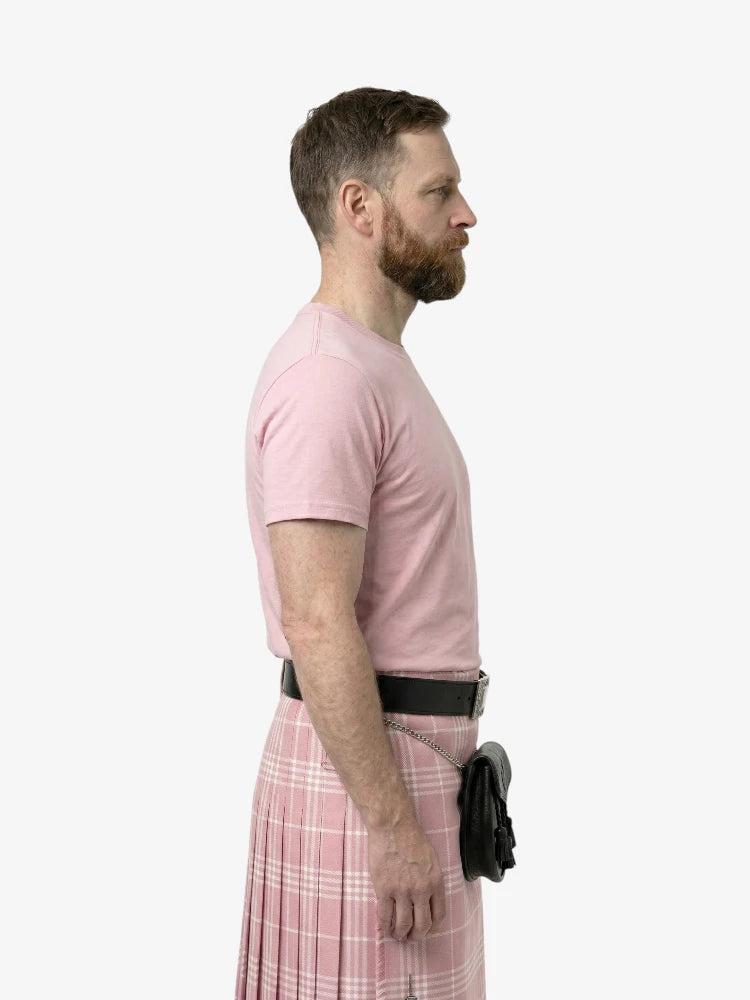 Man wearing a pink t-shirt and plaid kilt on a white background