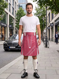 A man standing on a city sidewalk wearing a white t-shirt, a pink kilt with white geometric patterns, white knee-high socks, and black leather shoes. A black Mercedes-Benz car and a bicycle are visible in the background of the street scene.