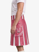 A person wearing a pink faux-leather kilt with white vertical stripes, white suspenders, and a front flap pocket with white drawstrings, shown against a light gray studio background.