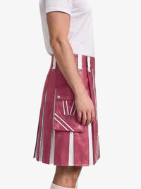 A side view of a person wearing a pink and white vertically striped pleated leather kilt with white suspenders and a matching pocket, paired with a white t-shirt.