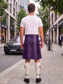 A man viewed from behind wearing a purple leather kilt with lace-up back detailing, a white t-shirt, white knee-high socks, and black shoes, standing on a city sidewalk.