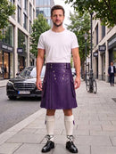 A man stands on a city sidewalk wearing a white crew-neck t-shirt, a pleated purple leather kilt with silver metal grommets, white knee-high socks, and black leather lace-up shoes. The background shows a street with buildings, a black Mercedes-Benz car, and a bicycle.