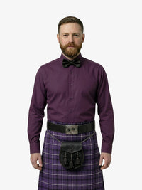 Man wearing a purple shirt, bow tie, and tartan kilt on a white background
