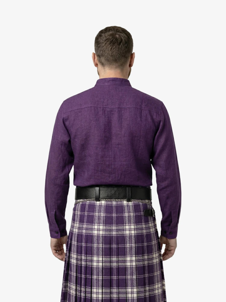 Man wearing a purple shirt and tartan kilt on a white background