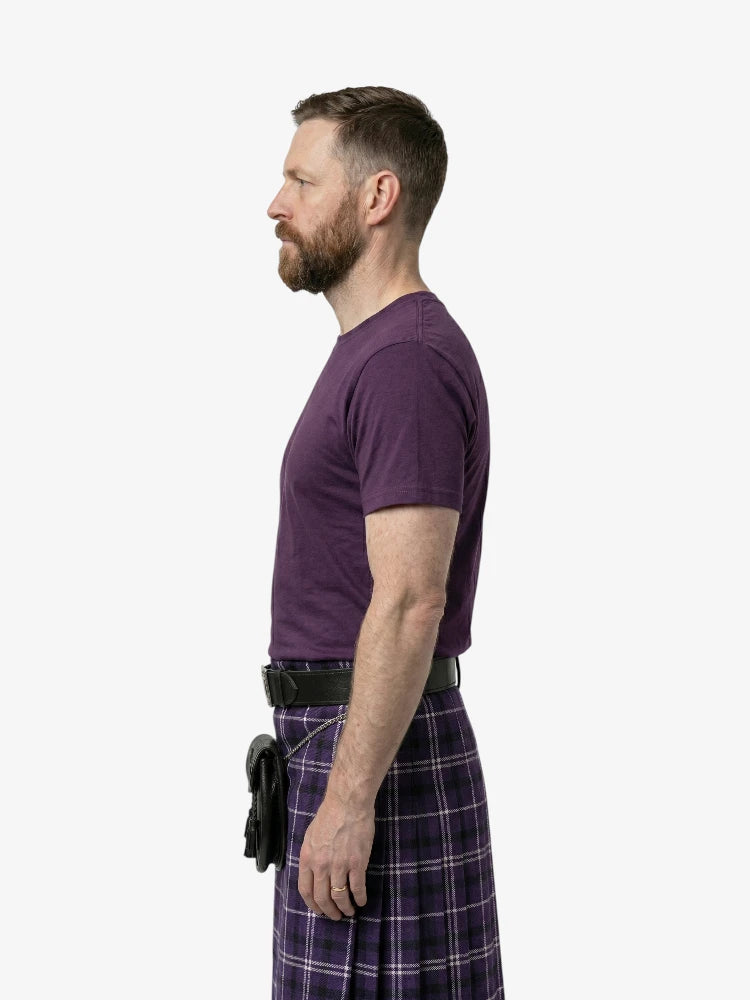 Man wearing a purple t-shirt and plaid kilt on a white background