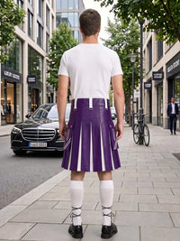A man standing on a city sidewalk, photographed from behind, wearing a white T-shirt and a purple pleated kilt with white vertical stripe panels, white knee-high socks, and black shoes. Buildings, trees, a black car, and a bicycle are visible in the background.