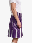 A person wearing a purple and white vertically striped leather kilt with silver metal hardware, paired with a white t-shirt, shown from the side against a light gray background.