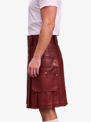 A man wearing a burgundy faux-leather kilt with pleated detailing and silver snap buttons, paired with a white t-shirt, shown from a side profile against a light gray background.