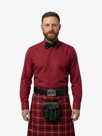 Man wearing a red shirt, bow tie, and tartan kilt on a white background