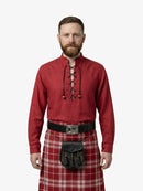 Man wearing a red shirt with lace-up front and a tartan kilt on a white background