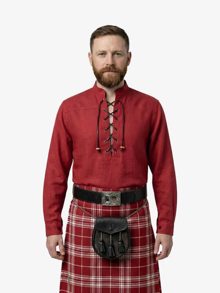 Man wearing a red shirt with lace-up front and a tartan kilt on a white background