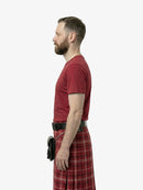 Man wearing a red t-shirt and plaid kilt on a white background