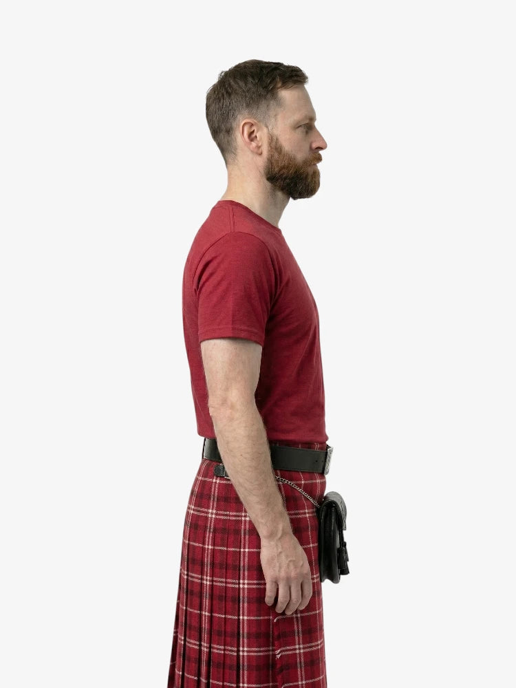 Man wearing a red t-shirt and plaid kilt on a white background