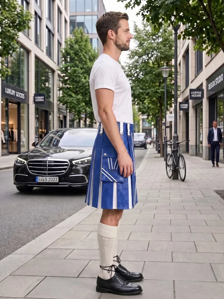 A man stands on a city sidewalk wearing a white short-sleeve T-shirt and a blue-and-white vertically striped kilt-style skirt, paired with cream knee-high socks and black leather shoes. Buildings, trees, a parked black car, and a bicycle are visible in the urban street setting.