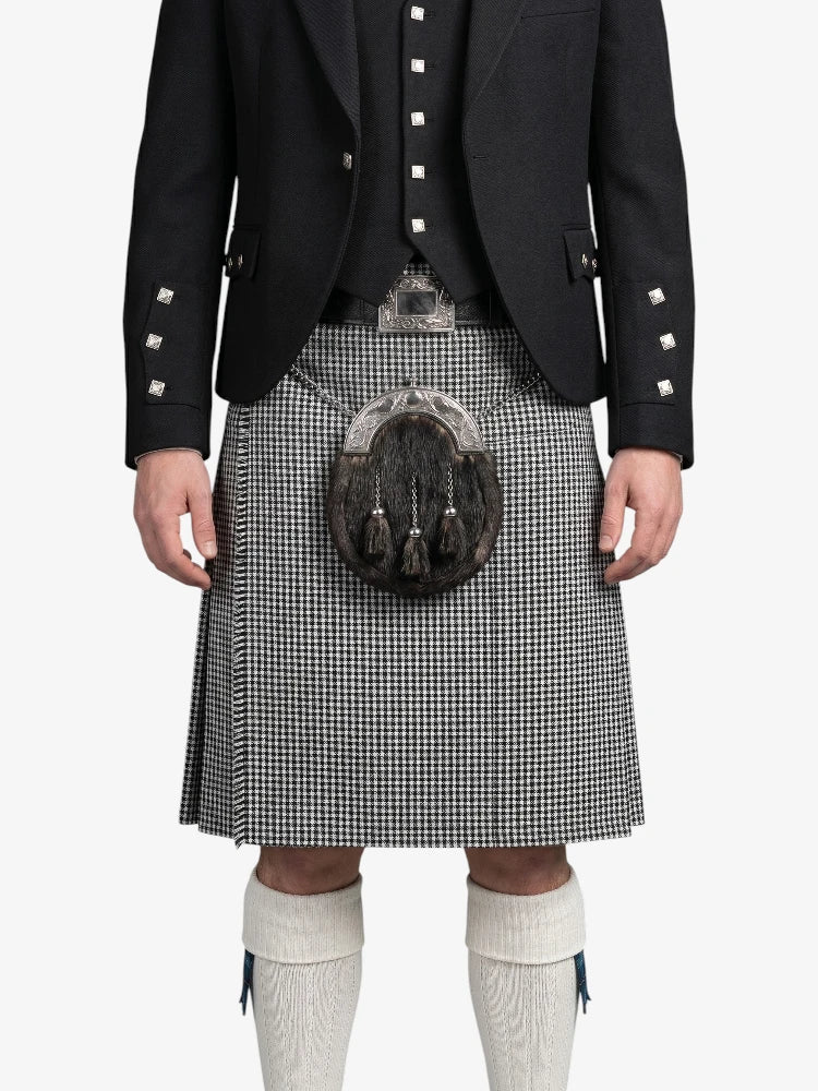 Person wearing a black jacket with white buttons, a kilt, and white knee-high socks on a white background