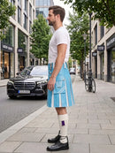 A man standing on a city sidewalk wearing a light blue and white striped kilt, a white t-shirt, white knee-high socks, and black leather shoes. A black Mercedes-Benz car and a bicycle are parked on the street behind him.