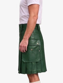 A man wearing a dark green faux-leather kilt with multiple flap pockets and brass button details, paired with a white t-shirt, shown from the side against a light gray background.