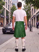 A man viewed from behind wearing a bright green leather pleated kilt, a white t-shirt, white knee-high socks, and black shoes, standing on a city sidewalk.