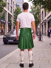 A man viewed from behind wearing a bright green leather pleated kilt, a white t-shirt, white knee-high socks, and black shoes, standing on a city sidewalk.