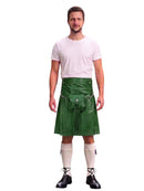 A man modeling a green faux-leather kilt with a matching belt and pouch, styled with a white t-shirt, white knee-high socks, and black shoes against a white background.