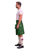A man shown in profile wearing a green leather kilt with multiple pockets, a white t-shirt, white socks with purple fringe, and black shoes, against a plain white background.