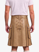 A person shown from the back wearing a tan pleated faux-leather kilt with a lace-up front, side cargo pockets, and silver-tone hardware, paired with a light pink t-shirt.