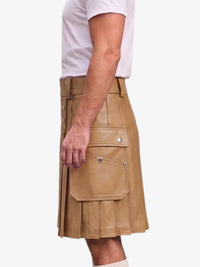A side view of a model wearing a tan faux-leather kilt with pleated detailing and flap pockets, paired with a white t-shirt against a light gray background.