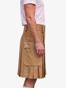 A person wearing a tan pleated leather kilt with flap pockets and a belt, paired with a white t-shirt, shown from the side against a light gray background.