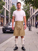 A man standing on a city sidewalk wearing a beige kilt with a front pouch pocket, a white t-shirt, white knee-high socks, and black leather shoes. Buildings, trees, and a black Mercedes-Benz car are visible in the background.