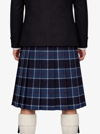 Person wearing a dark coat and blue plaid kilt with white knee-high boots on a white background